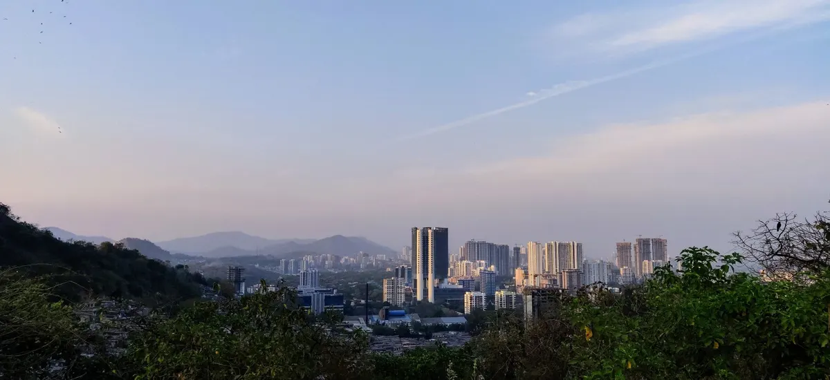 A wide evening view over a hill settlement and the city beyond.