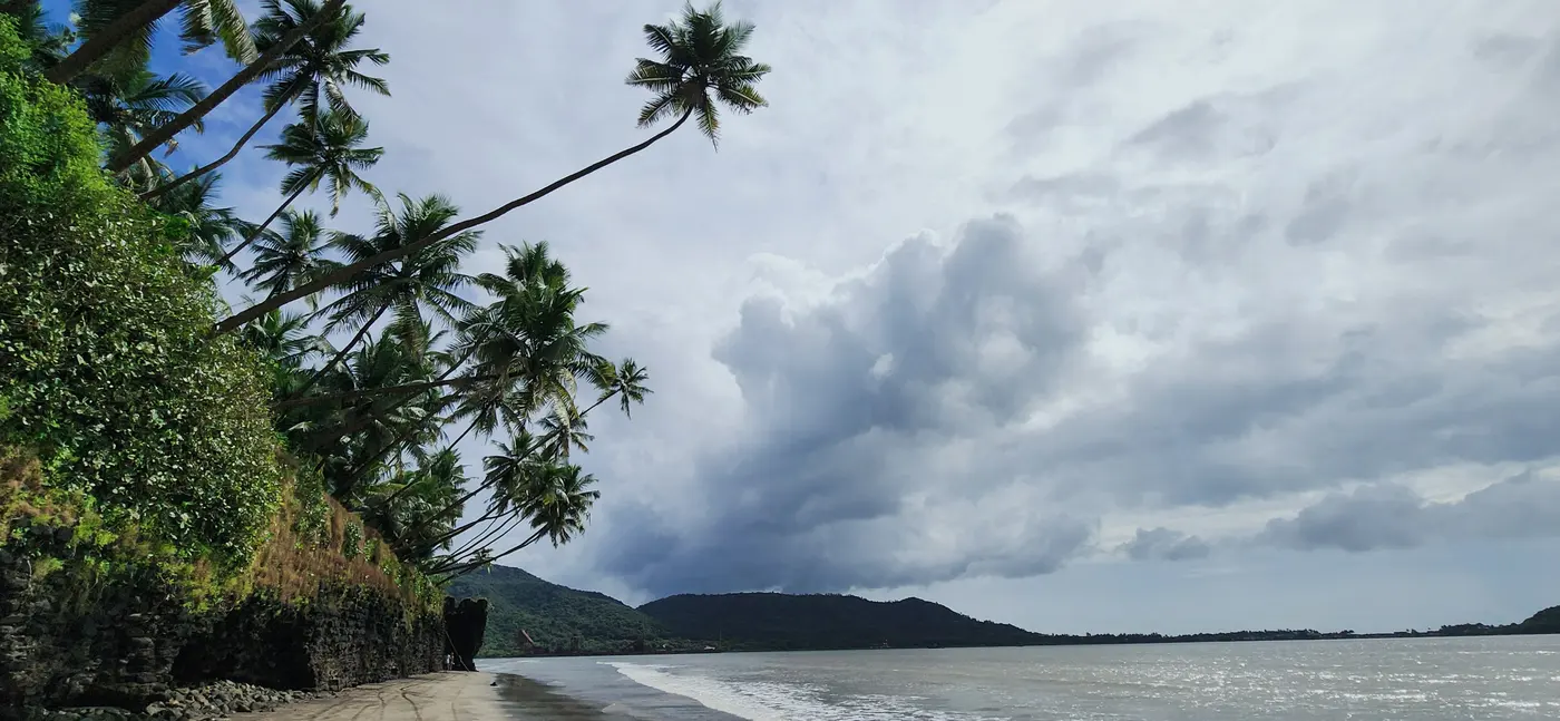 An empty beach and a headland under a cloudy sky, with sea to the horizon.