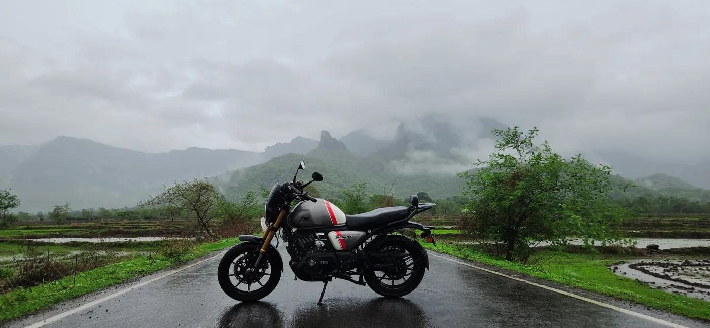 Musafir parked in the middle of an empty wet road, flooded fields either side and hills in the mist ahead.