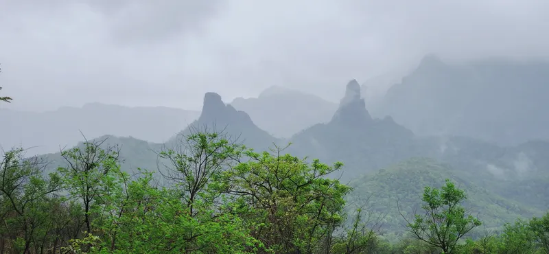 Two rock pinnacles standing above forested hills in monsoon cloud.