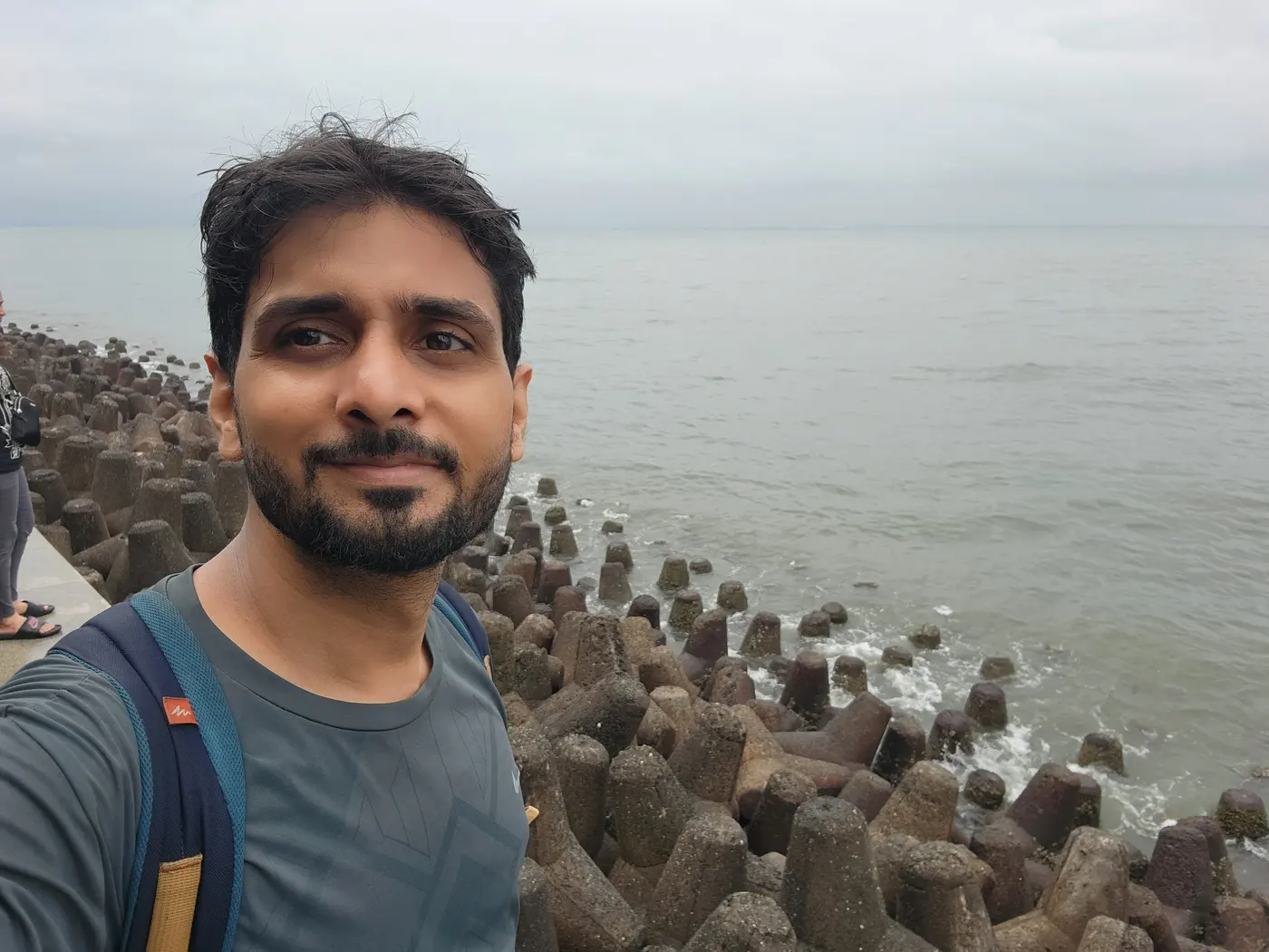 Me smiling in front of the grey sea and concrete tetrapods on a cloudy day.