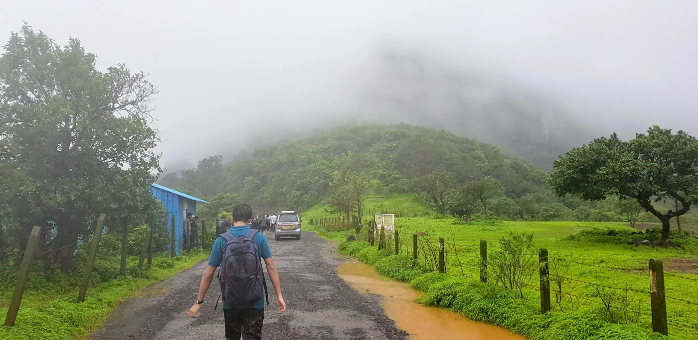 A wet road with a man in a backpack walking towards a hill lost in cloud.