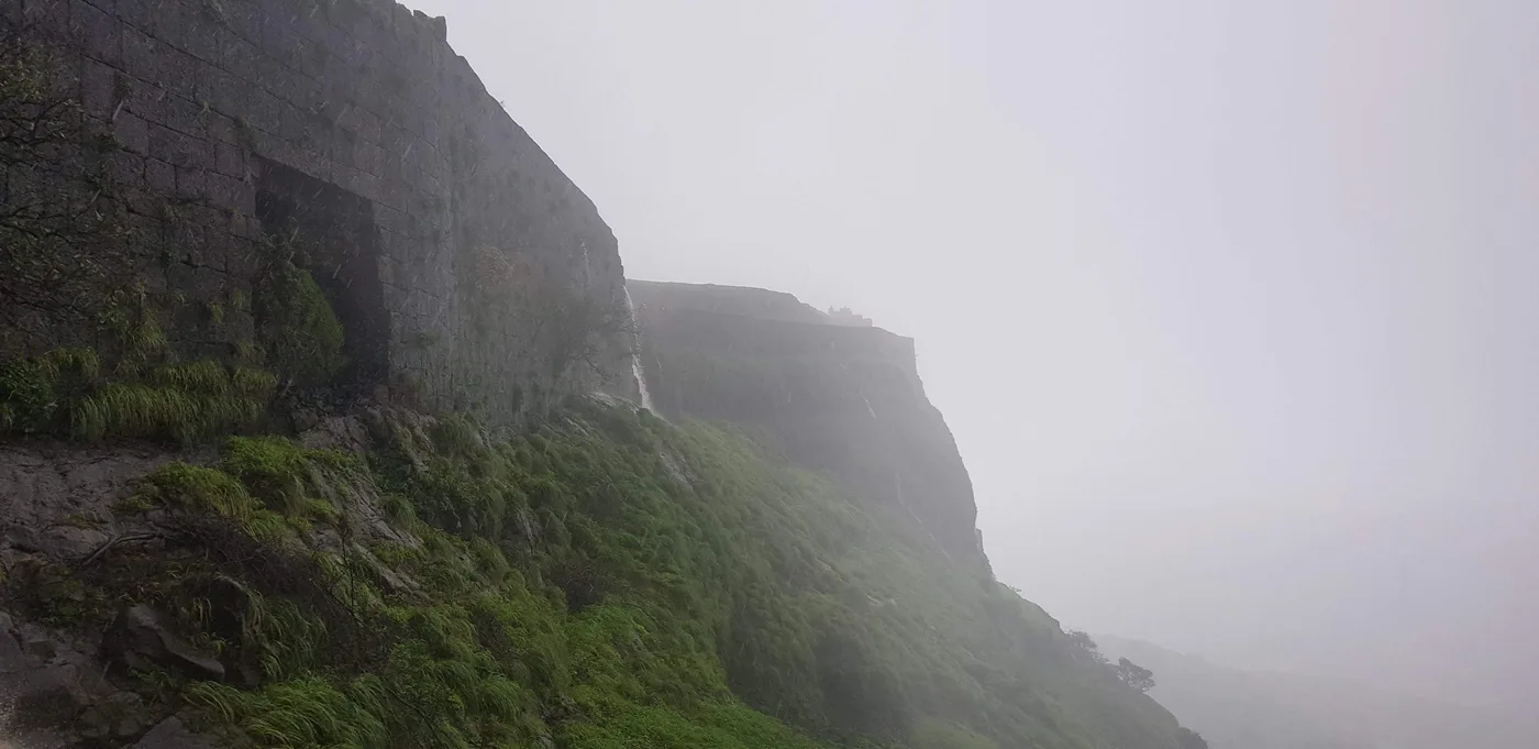 A grey fort wall rising out of green slopes and thick cloud.